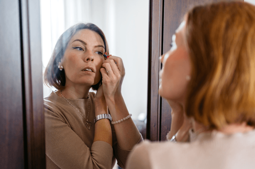 Brunette woman applying eyeliner in the mirror