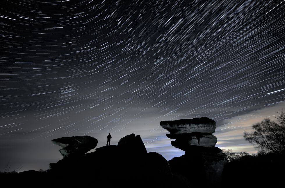 \u200bA man watches a meteor during the Geminid meteor shower over Brimham Rocks, in North Yorkshire