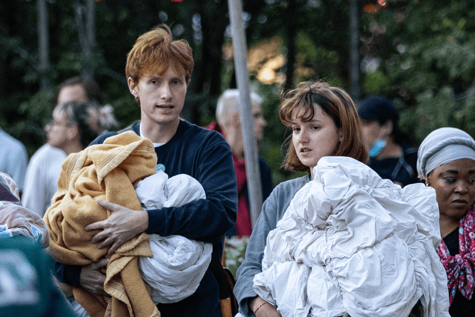 Volunteers hold blankets and look on at the migrant camp