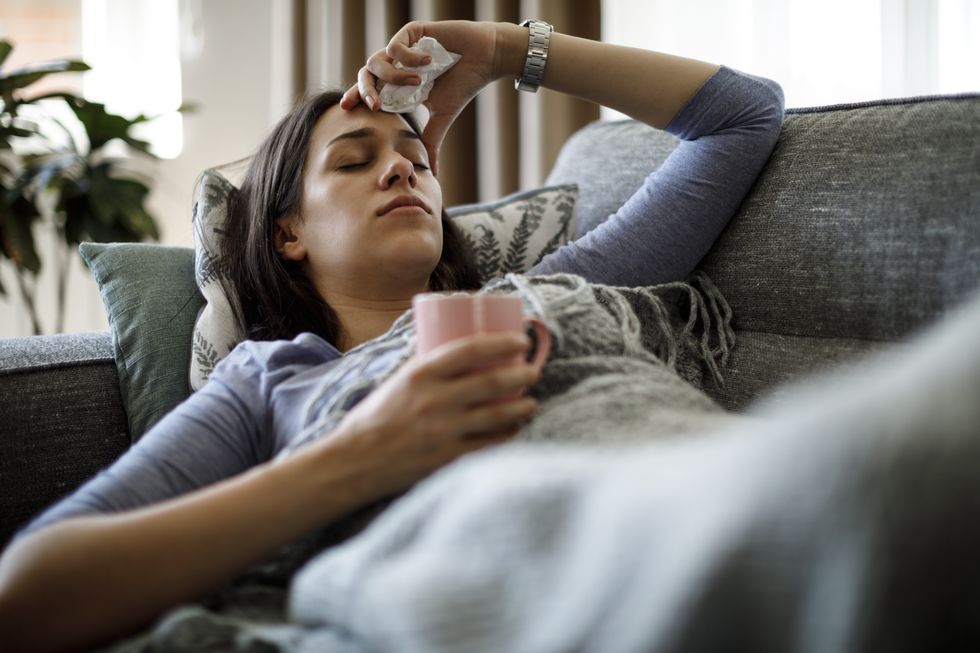 Woman with the flu holding her head and wrapped in a blanket on the sofa